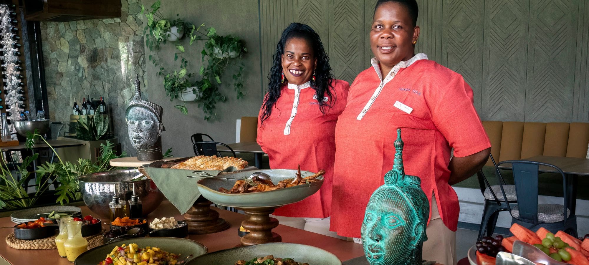 Two smiling Tanda Tula team members preparing and presenting a delicious safari meal.