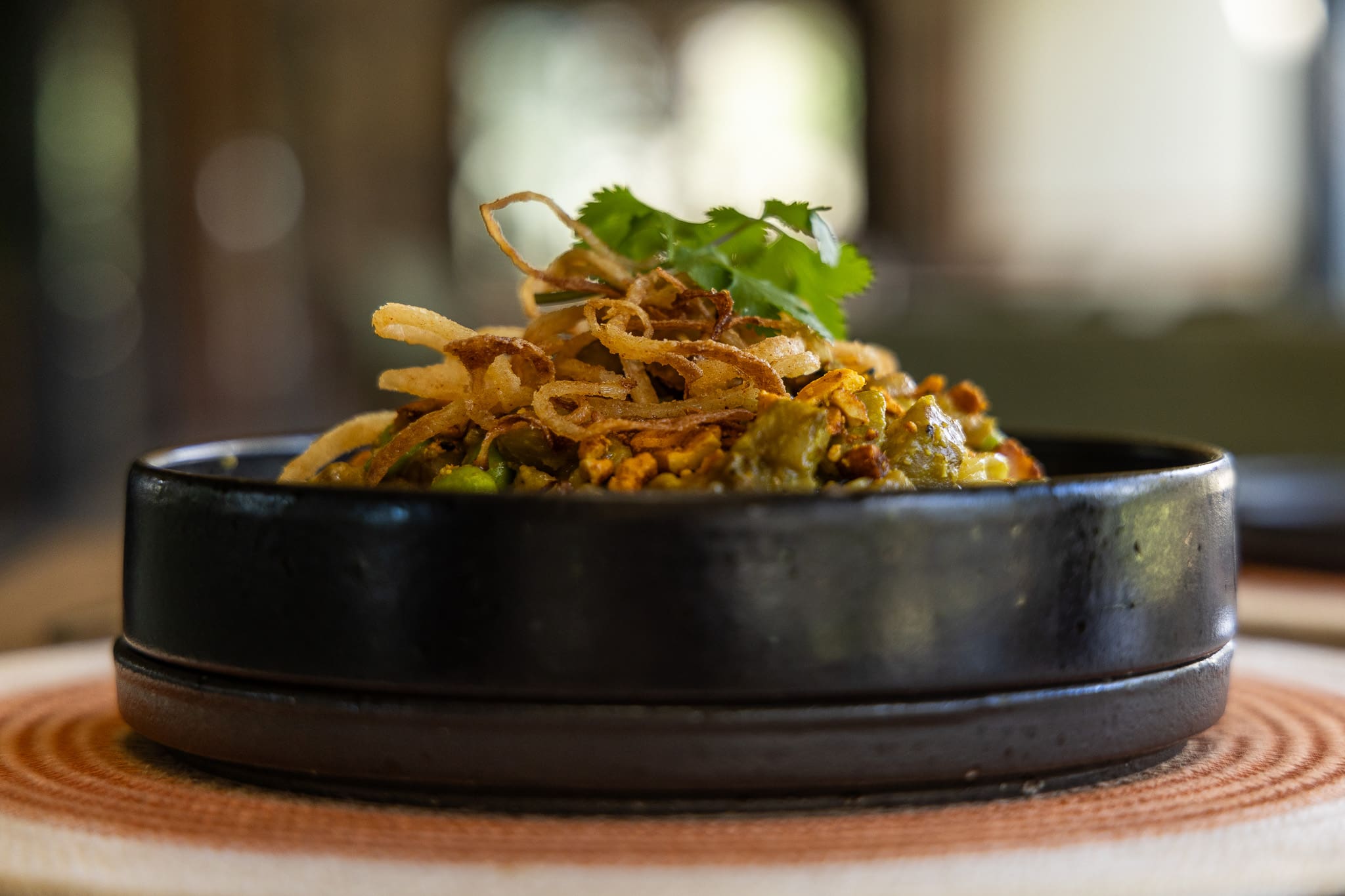 A beautifully plated dish featuring crisp fried onions, fresh herbs, and a vibrant vegetable medley, artfully served in a handcrafted ceramic bowl at Tanda Tula’s safari lodge in the Timbavati.