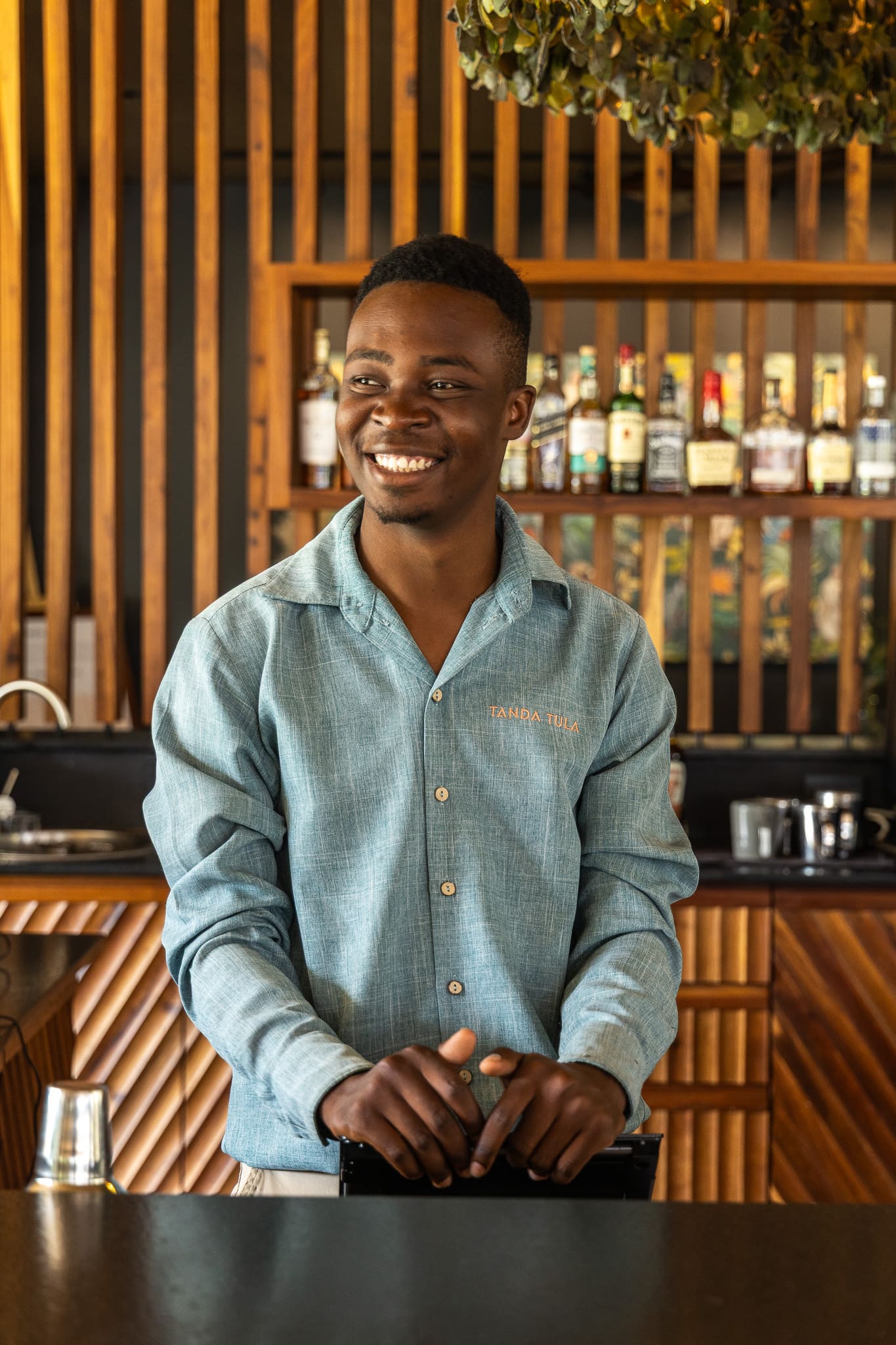Allied Mathebula smiling behind the bar at Tanda Tula, representing the next generation of the lodge’s family legacy.