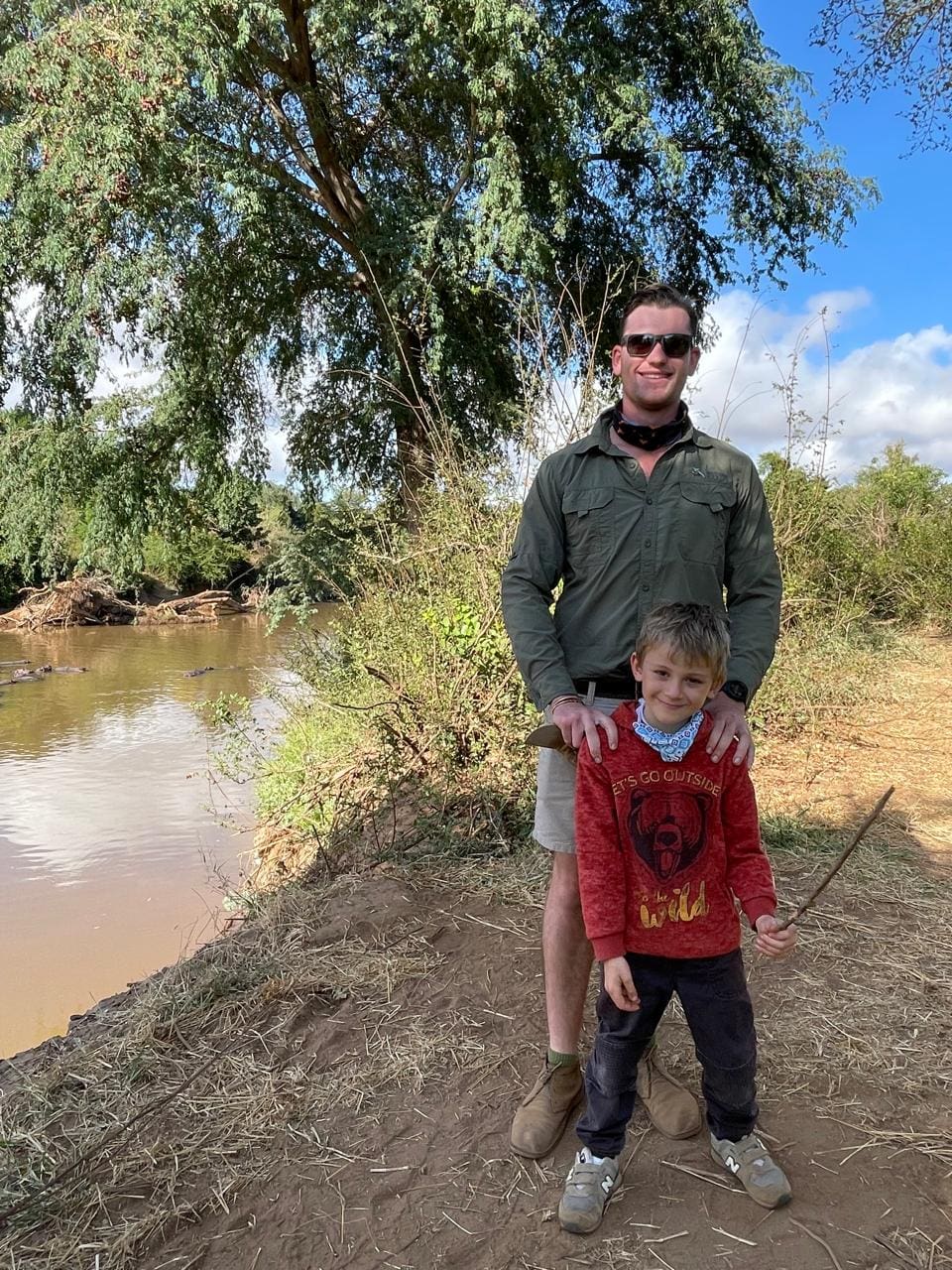 Field guide Tristan Allan-Reynolds standing with a young guest beside a river in Pafuri during a walking safari.